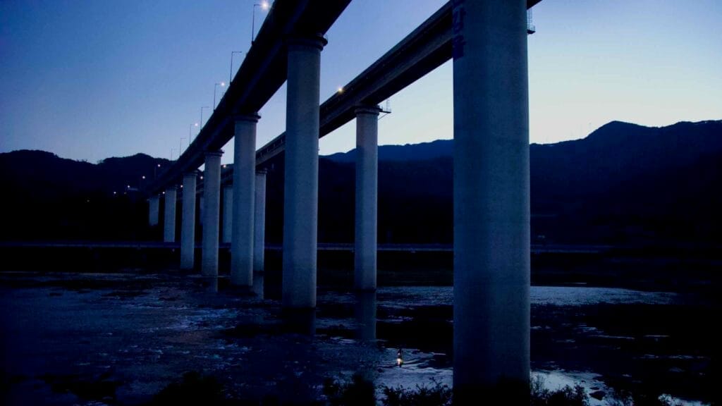 Twilight view of bridge pillars spanning the Seomjin River with mountains in the distance.
