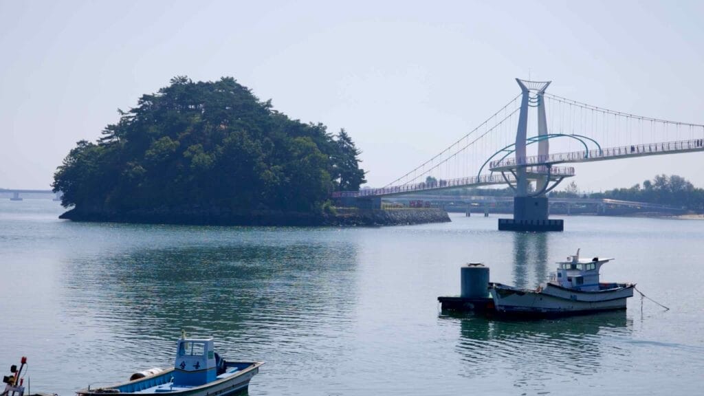 A view of Byeol Heneun Bridge connecting Baealdo with the mainland, with fishing boats floating in the calm waters where the Seomjin River meets the South Sea.