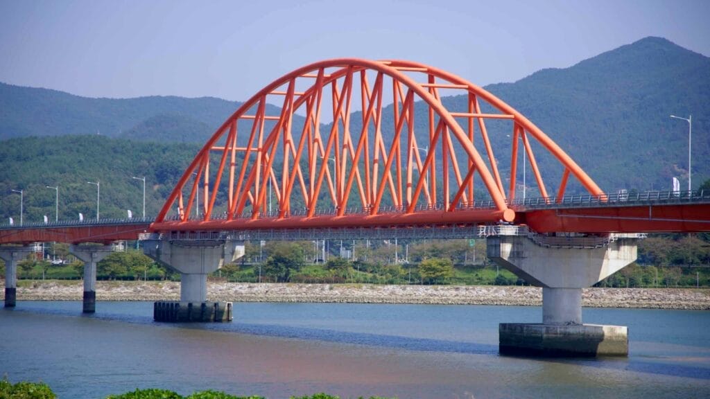 A detailed view of the Seomjingang Grand Bridge, a red arch bridge spanning the Seomjin River.