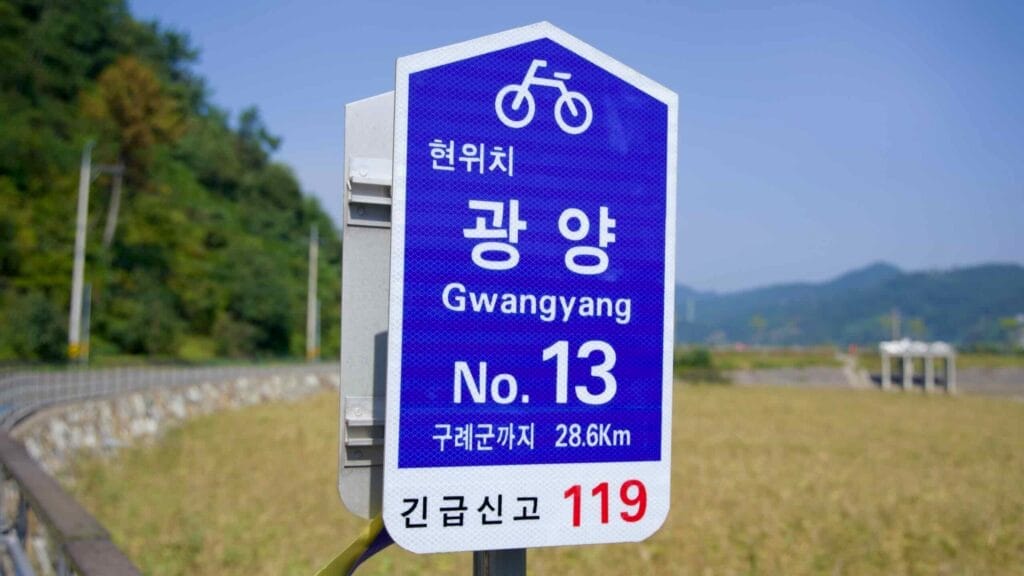 A route marker on the Seomjingang Bicycle Path provides distance and emergency contact details.
