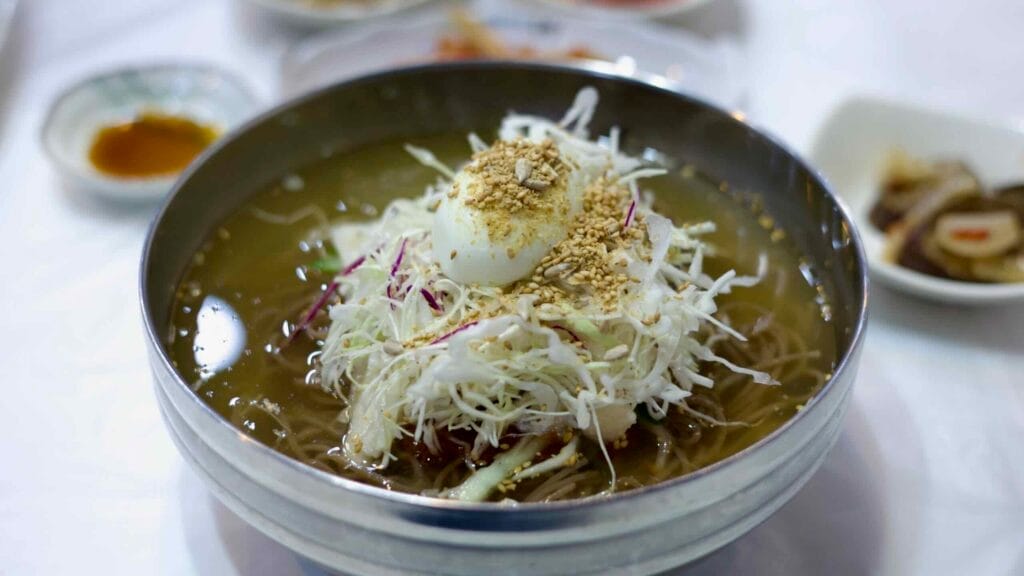 A bowl of naengmyeon, Korean cold noodles with shredded cabbage, a boiled egg, and sesame seeds.