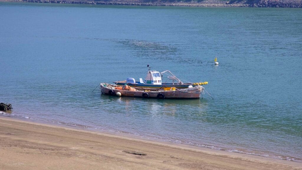 A weathered fishing boat floats on the calm waters of the Seomjin River near a sandy shoreline.