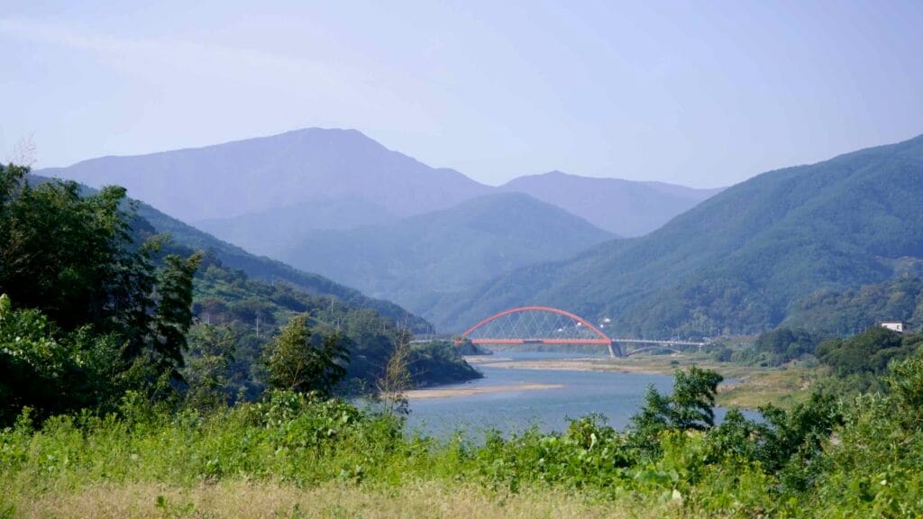 Scenic red arch bridge with lush green mountains and the winding river below.