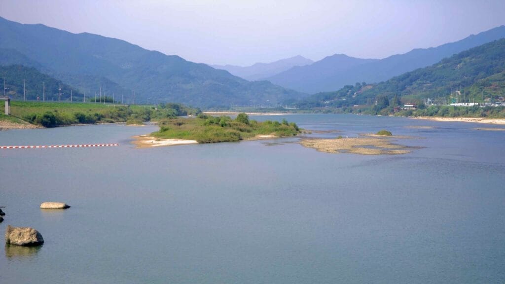 A panoramic view of the Seomjin River flowing through a wide valley, with small river islands and sandbanks.