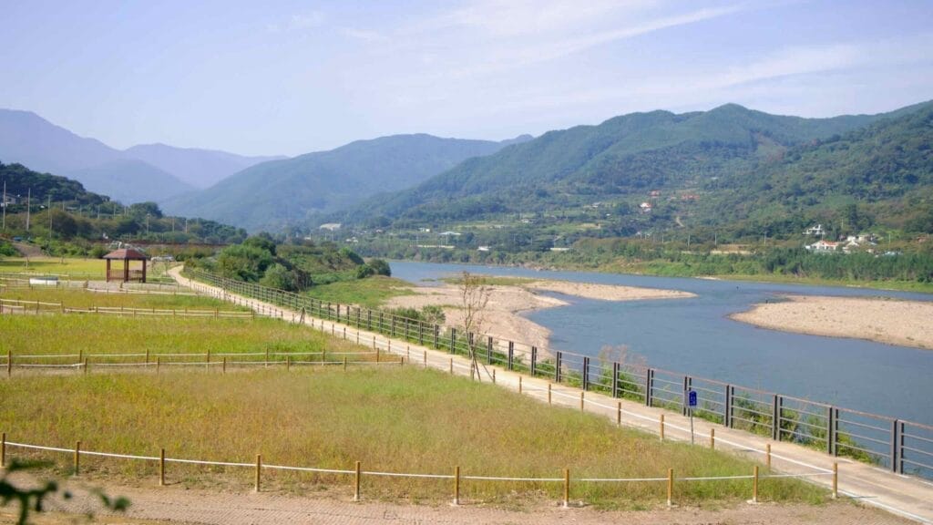 Seomjingang Bike Path with lush green mountains and a wooden pavilion.
