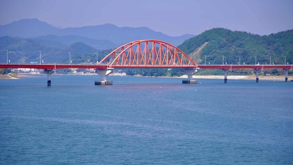 A view of the Seomjingang Grand Bridge, a red arch bridge spanning the Seomjin River.