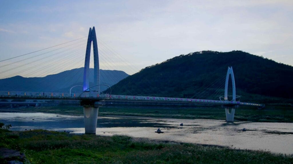 Toad Bridge, a modern cable-stayed pedestrian bridge, spans the Seomjin River in the fading daylight.