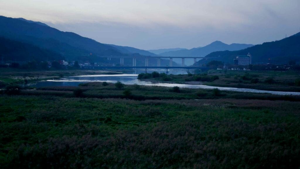 Twilight over the Seomjin River valley, with reflections, bridges, and villages among rolling mountains.