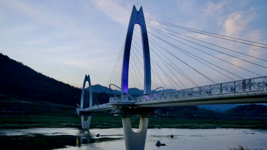 Toad Bridge glows with soft purple illumination at twilight, spanning the Seomjin River.