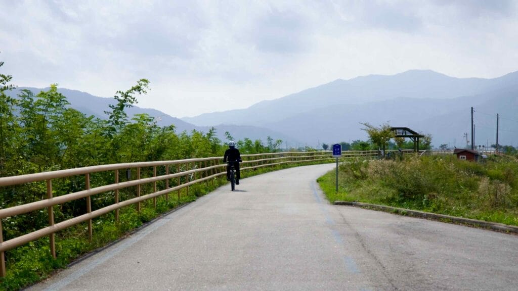 Lone cyclist on the Seomjingang Bike Path, surrounded by lush greenery and rolling mountains.