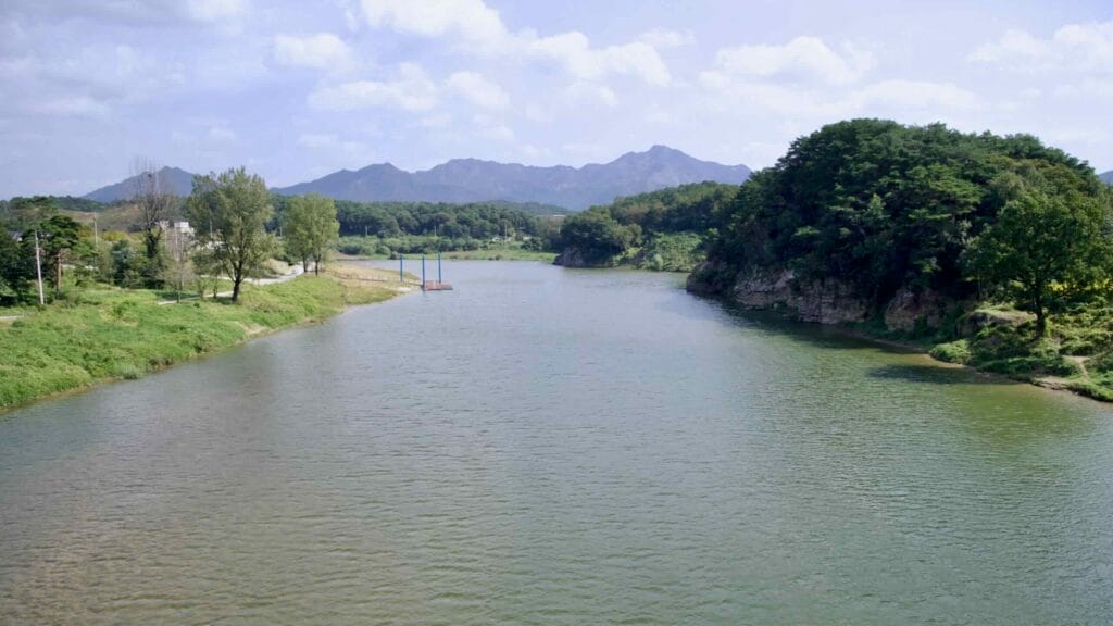 Serene Seomjin River with lush greenery, a small dock, and distant mountains along the Seomjingang Bike Path.
