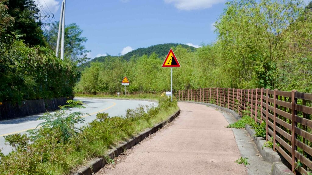Yeongsangang Bike Path next to a winding road, backed by mountains and greenery.