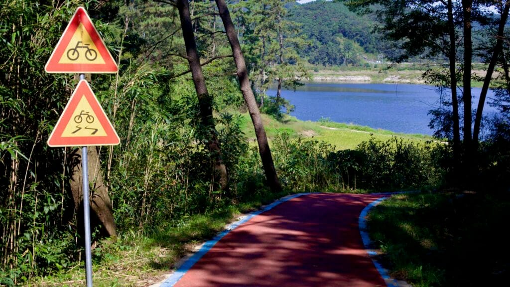 A winding bike path slopes toward the river with warning signs.