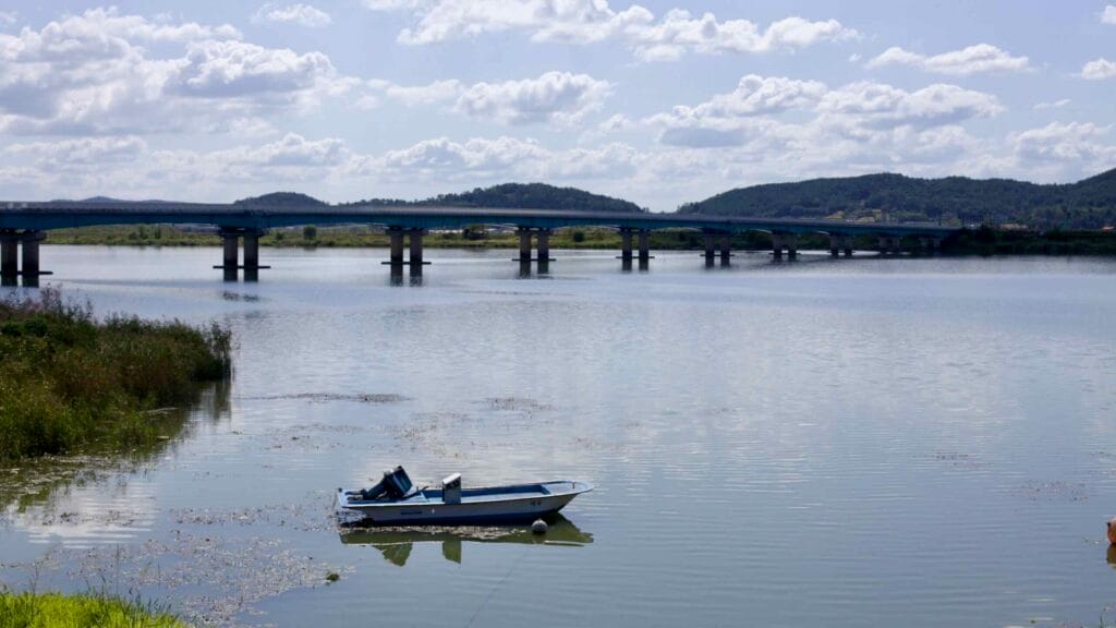 A small fishing boat floats near the riverbank of the Yeongsan River, with a modern bridge