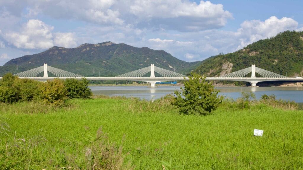Muyeong Bridge spanning the river, framed by rolling green hills and lush vegetation.