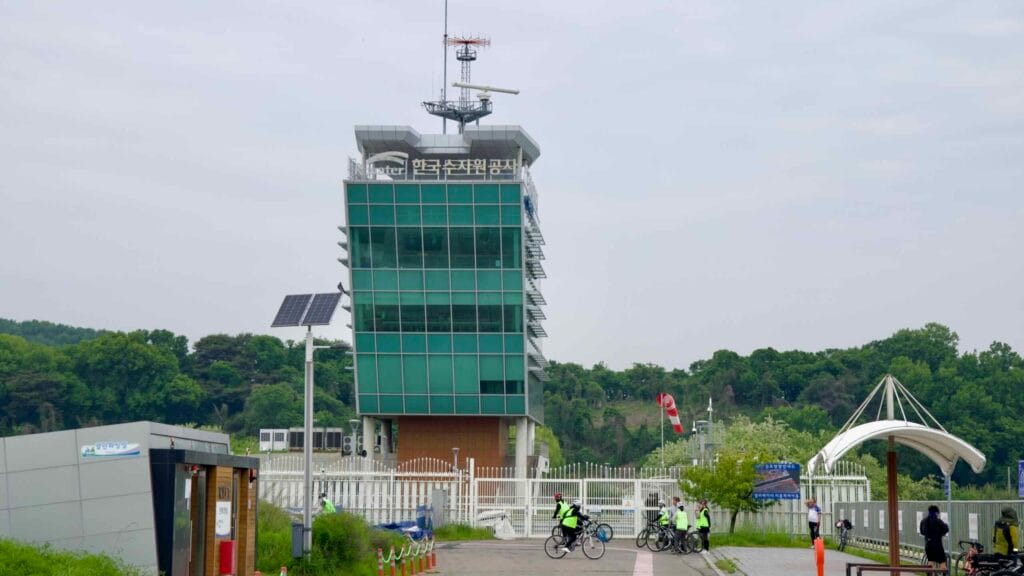 The Ara Hangang Lock control tower rises behind a group of cyclists at a rest area.