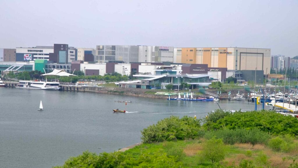Boats sail across the Gyeongin Ara Waterway near Ara Marina, with yachts docked below the Hyundai Premium Outlets and SSG.COM logistics complex.
