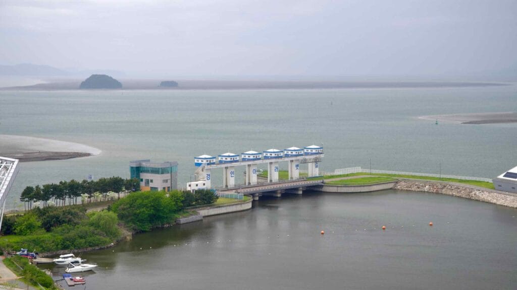 A close view of the Ara West Sea Lock, where the Gyeongin Ara Waterway meets the Yellow Sea, with small boats moored nearby and tidal flats and islets visible beyond the lock gate.