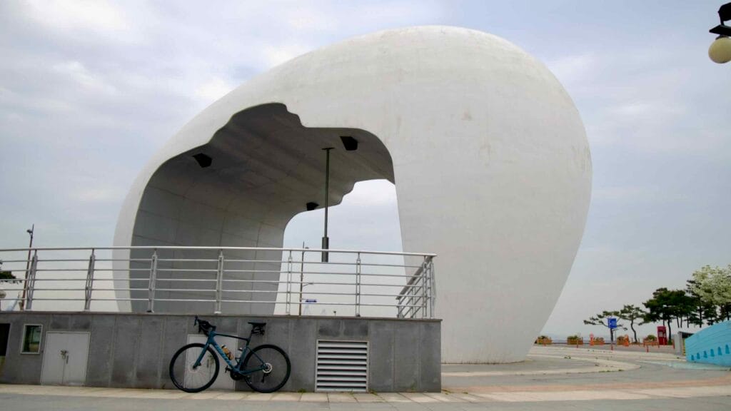 A road bike rests beneath the Jeongseojin Sunset Bell monument, where cyclists finishing the Ara Bicycle Path reach the symbolic end point of the Gyeongin Ara Waterway at the Yellow Sea.