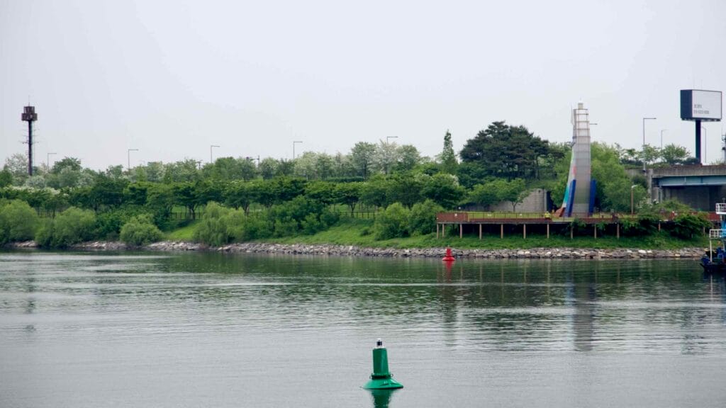 Duri Ecological Park lines the Ara Waterway with its greenery and observation deck, marked by a colorful tower sculpture near the canal’s edge.