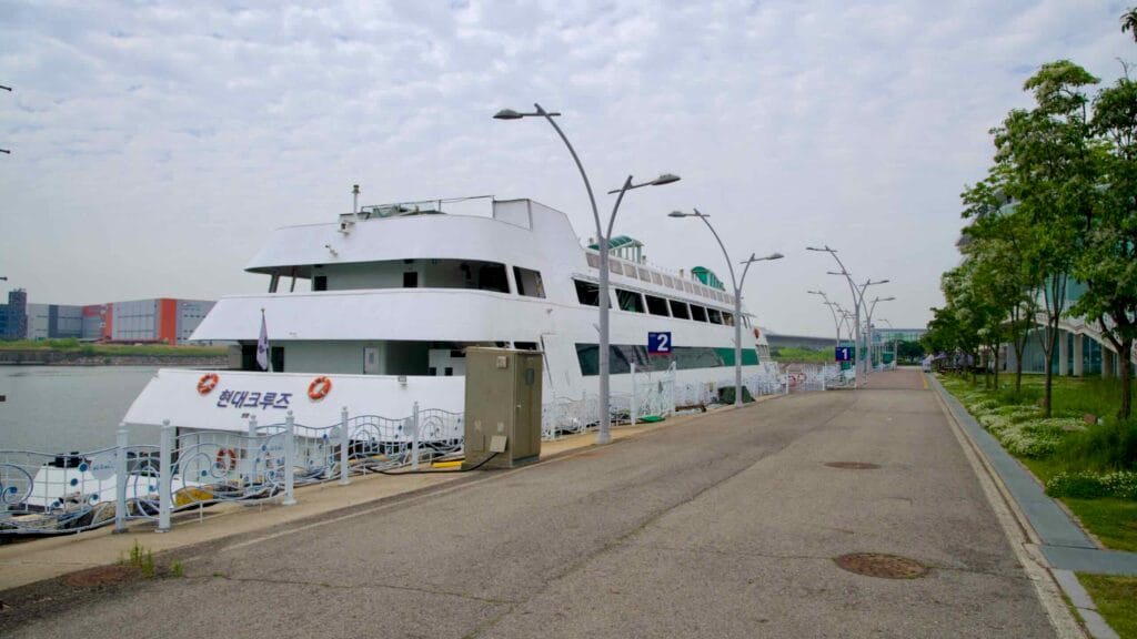 A Hyundai Cruise ship is moored at Pier 2 of the Ara Gimpo Passenger Terminal, offering river excursions along the Gyeongin Ara Waterway beneath a soft overcast sky.