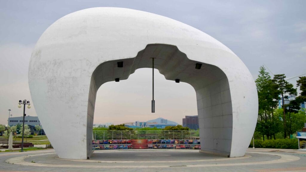 The Jeongseojin Sunset Bell monument frames a distant view of the horizon, with photo tiles and interpretive panels beneath marking this symbolic coastal gateway at the end of the Ara Waterway.