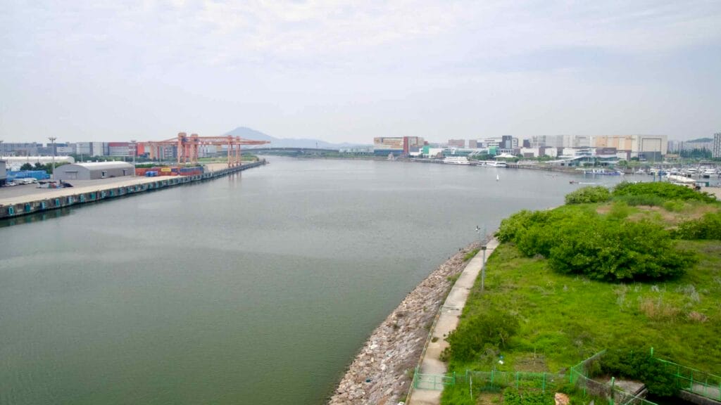 Looking east from Jeonho Bridge across the Ara Waterway, with Ara Marina, the Ara Gimpo Passenger Terminal, and the lock facility visible beside an industrial pier.