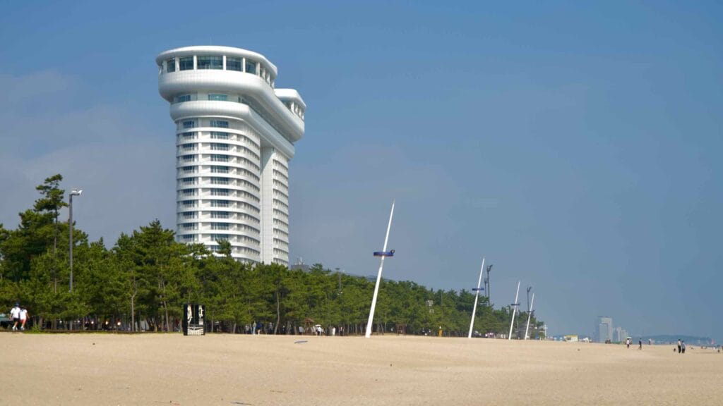 White tower overlooks Gyeongpodae Beach, where visitors enjoy the sandy shoreline.