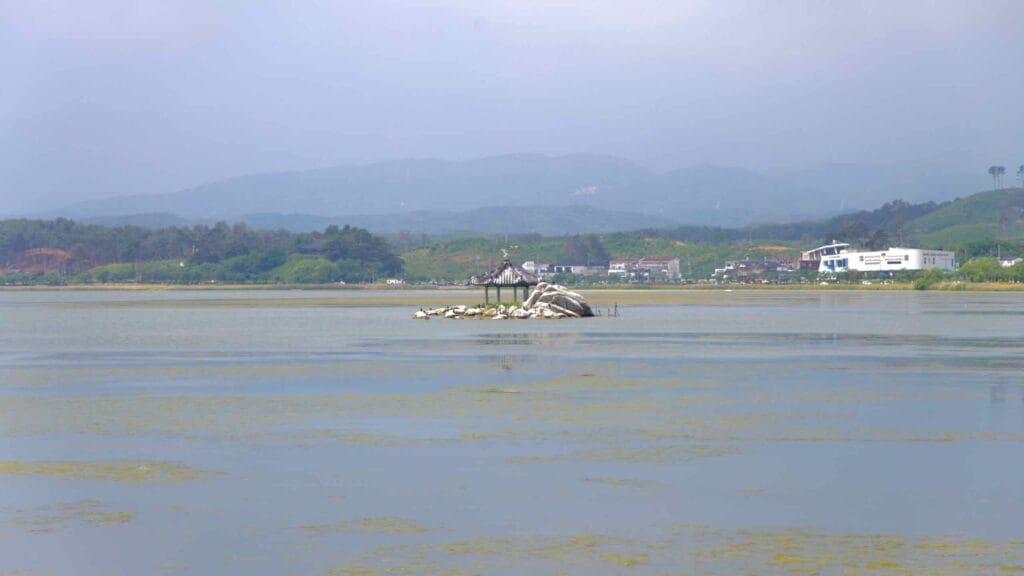 Small stone pavilion on an islet in Gyeongpo Lake, surrounded by still waters and distant mountains.