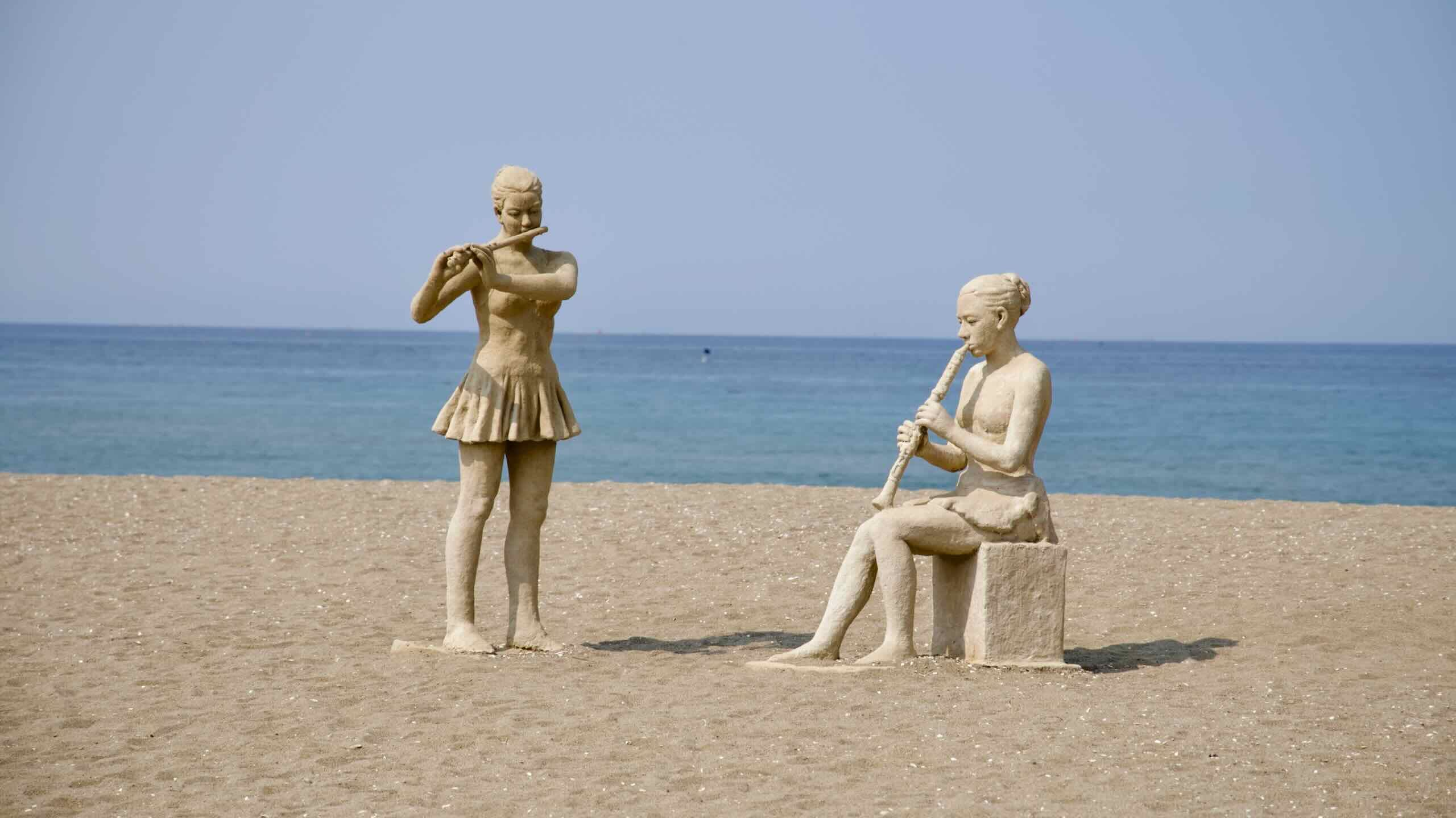 Two life-sized beachside statues, one standing with a flute and the other seated with a recorder, portray musicians playing to the sea on Deoksan Beach.
