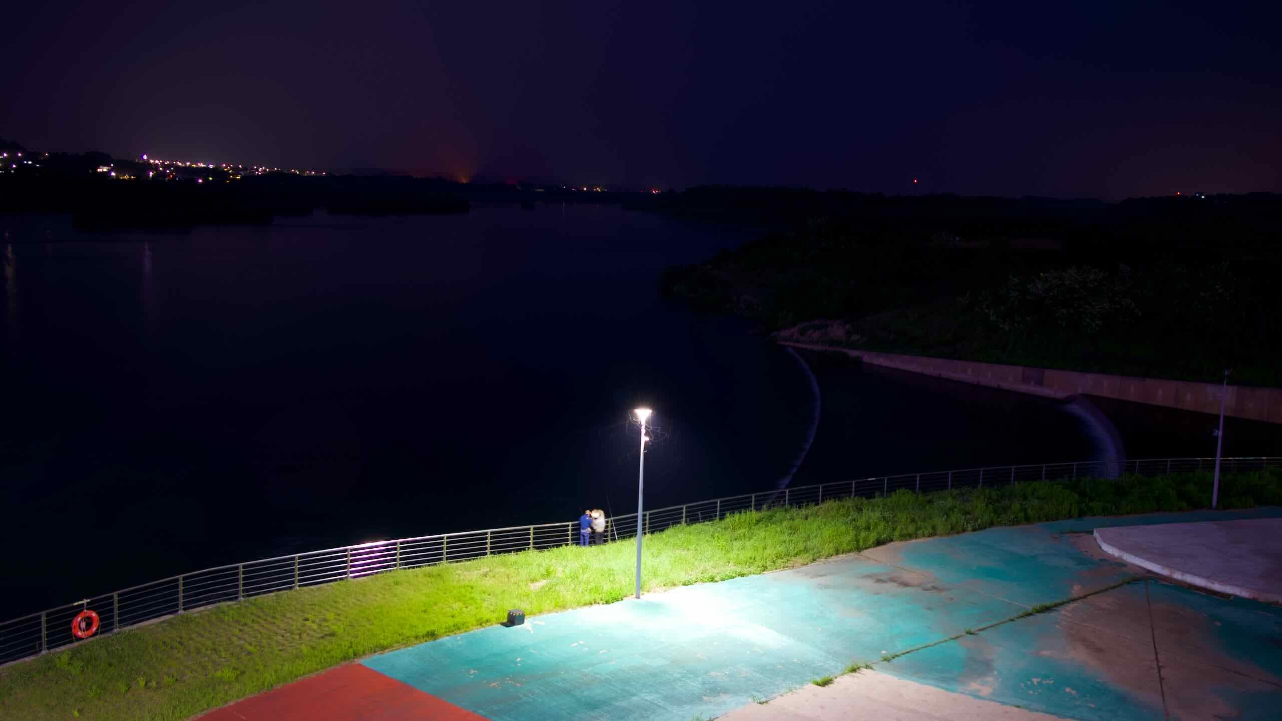 A couple stands beneath a streetlight overlooking the dark South Han River, captured from the riverside park near Yeoju Weir and its surrounding observation paths.