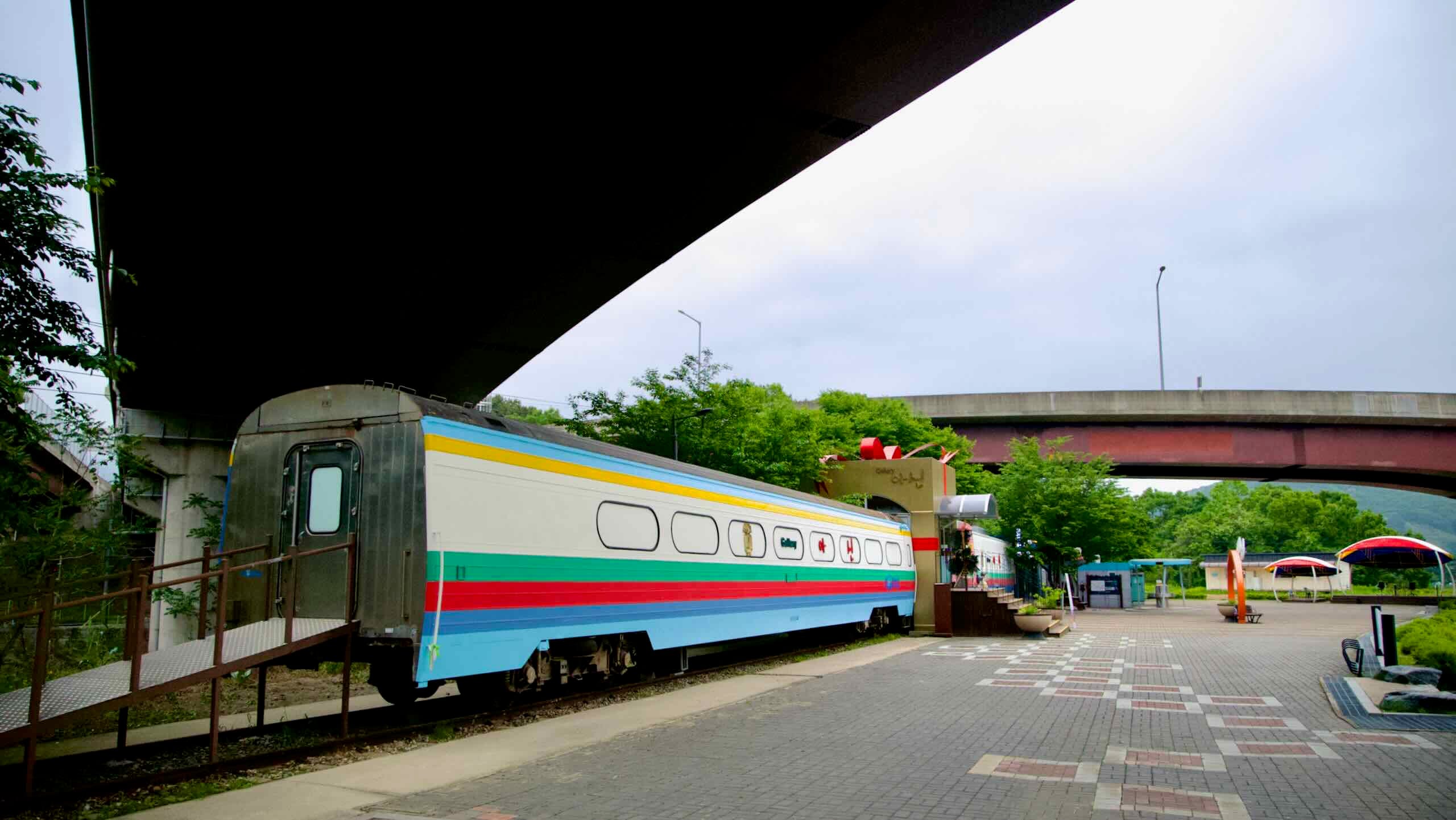 A decommissioned train car transformed into a gallery stands under a highway overpass in Asin Cultural Plaza, part of a creative reuse project in Yangpyeong.