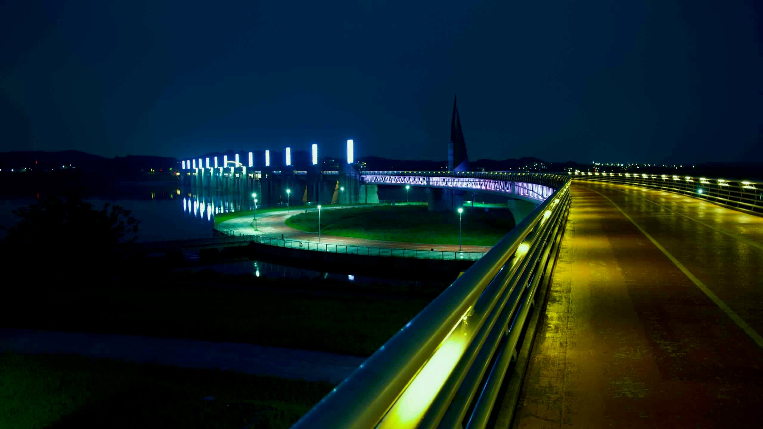 An elevated bike path curves toward Yeoju Weir and its observatory tower, where Sejong-inspired architecture and vivid lights overlook the South Han River.
