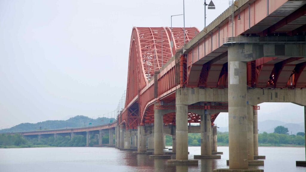 Banghwa Bridge’s dual steel spans and concrete pillars extend over the Han River, viewed from the riverside path near the Ara Hangang Lock, connecting Seoul and Incheon.