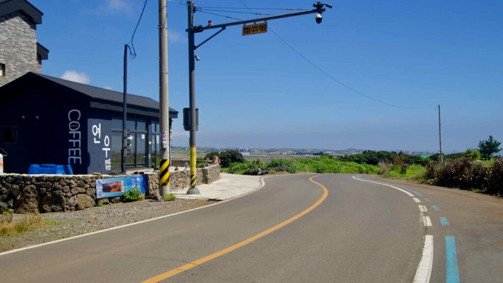 Roadside café and traffic camera on a coastal curve near Suwolbong, Jeju.