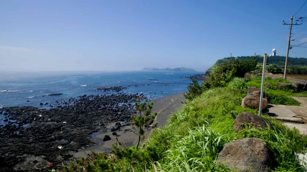 Clifftop view toward offshore islets and a distant radar dome near Suwolbong, Jeju.
