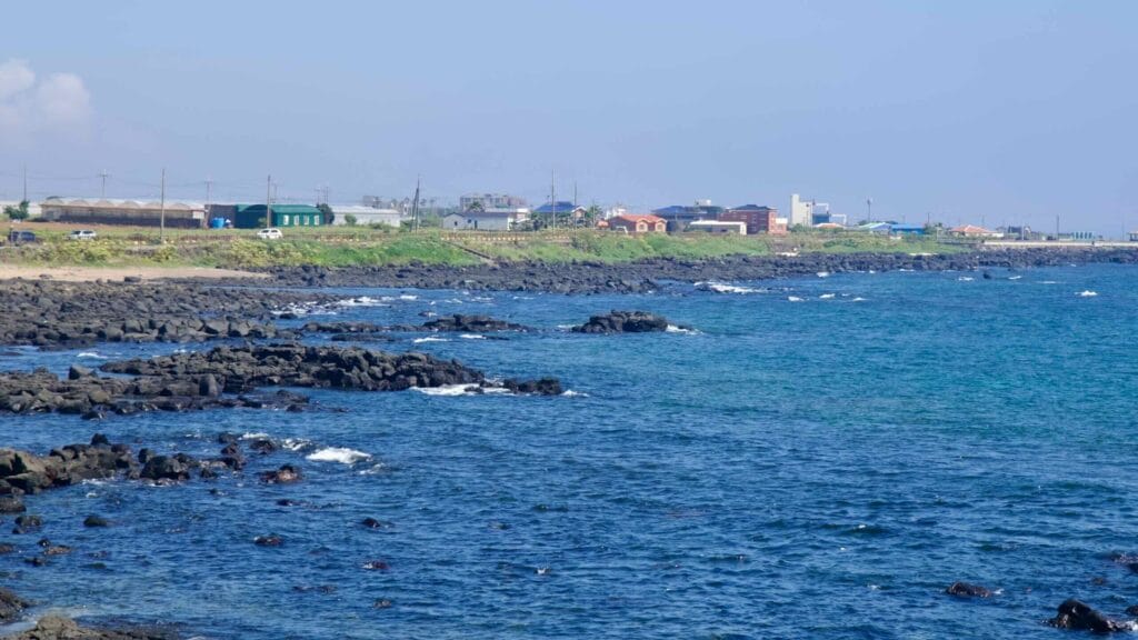 Waves over lava outcrops below fields and houses near Sindo Port, Jeju.