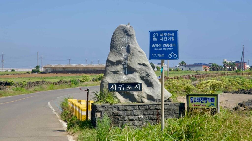 Seogwipo City border stone and bike‑route sign near Sindo on Jeju’s coast.