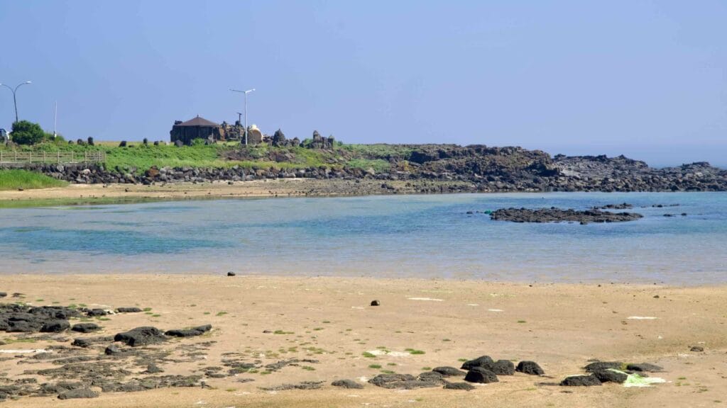 Quiet sandy cove with clear shallows and lava rocks near Sindo Port.