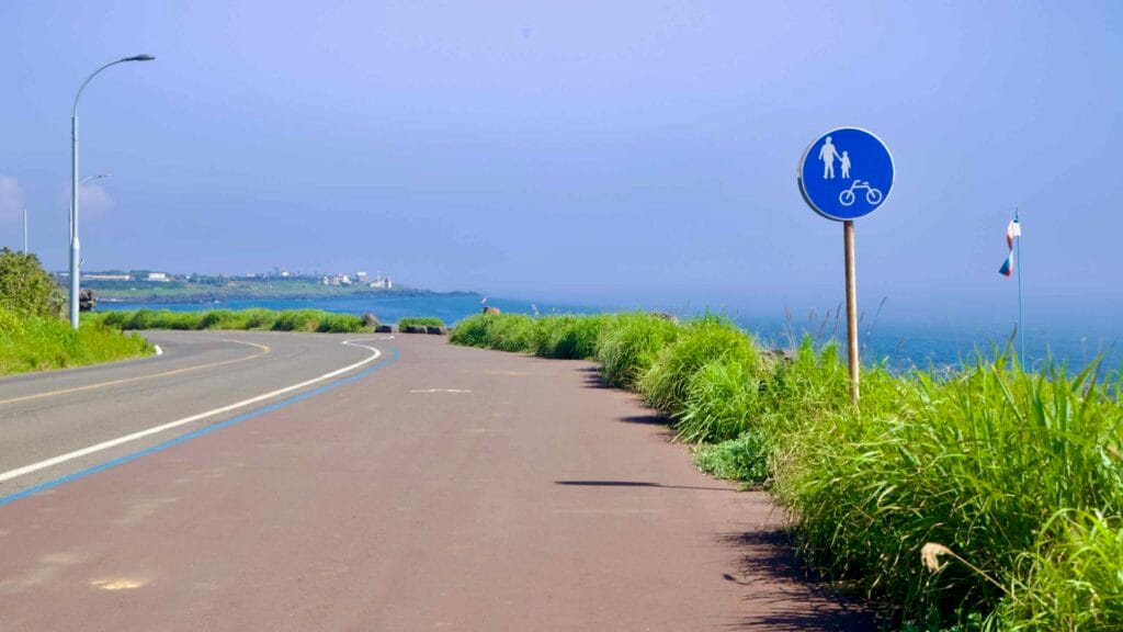 Shared‑path sign along Yeongnak Coastal Road overlooking Jeju’s rocky west shore.