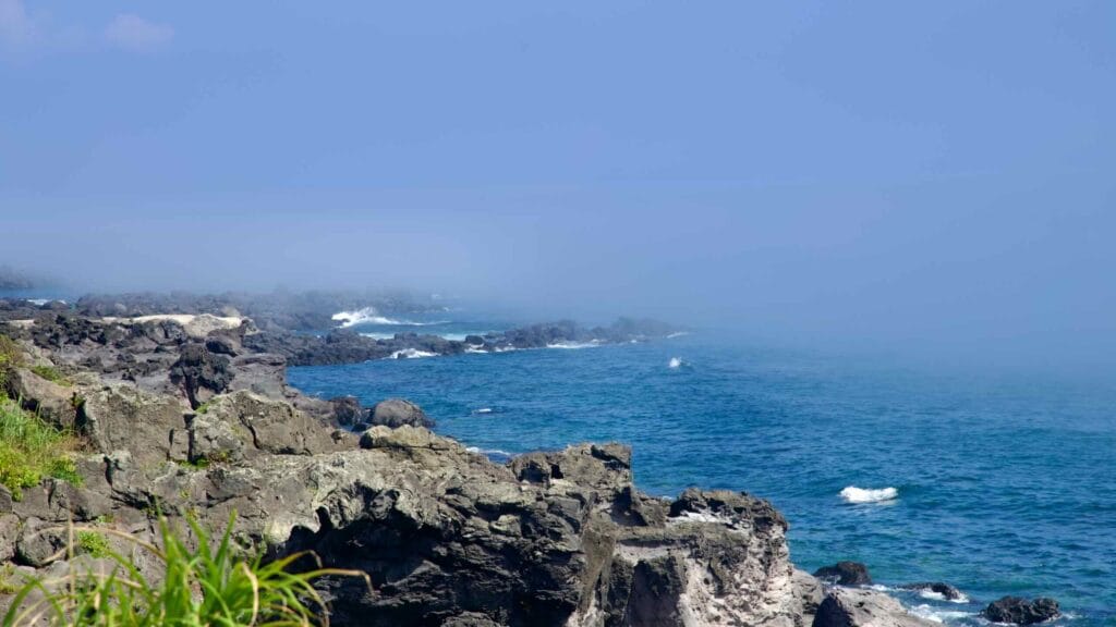 Sea fog over Jeju’s black‑rock Yeongnak coastline and layered volcanic outcrops.