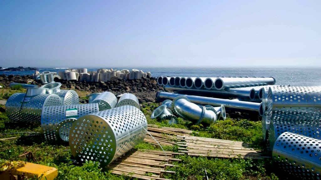Perforated cylinders and pipes staged for coastal works at Yeongnak’s basalt shore.