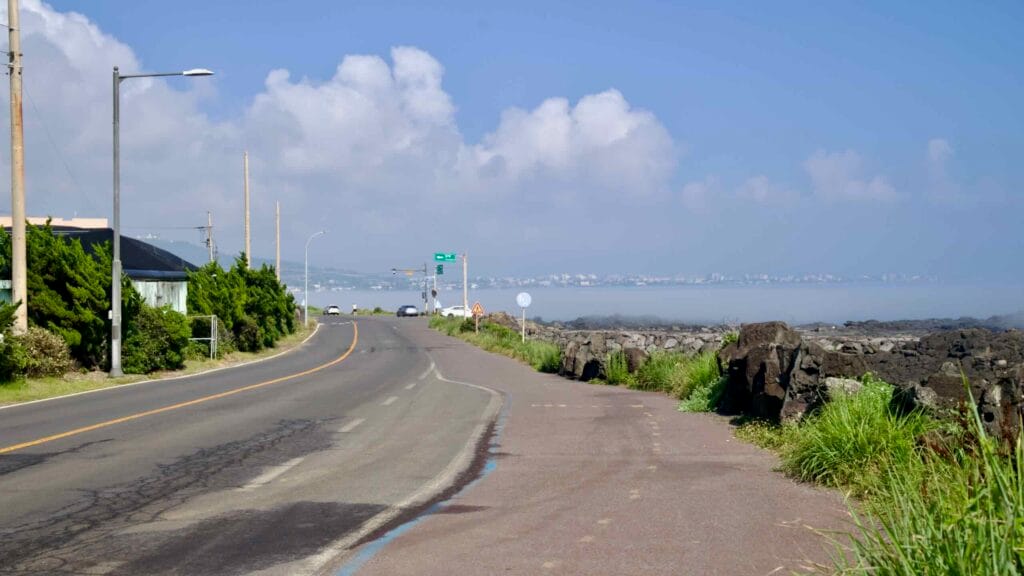 Roadside view toward a junction with seawall and distant skyline over sea fog.