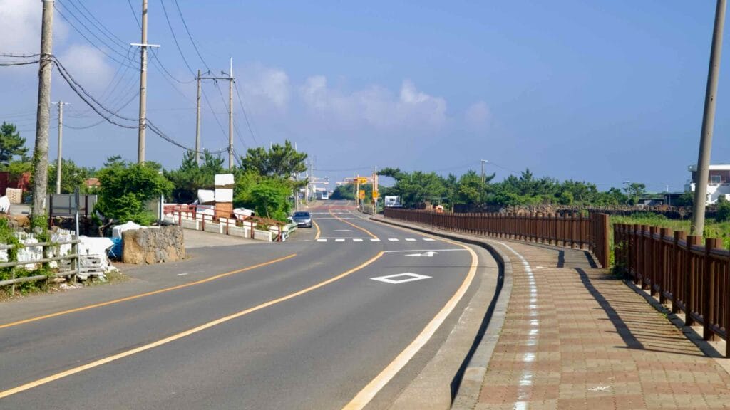 Yeongnak coastal road with blue bike line and brick walkway on Jeju’s shore.