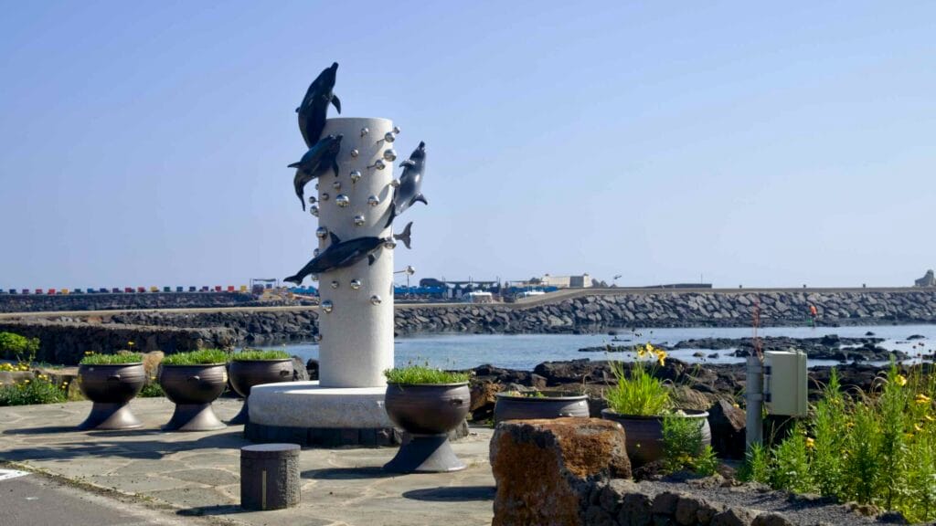 Dolphin sculpture by the harbor at Dongil‑ri Port overlooking tetrapods and pools.