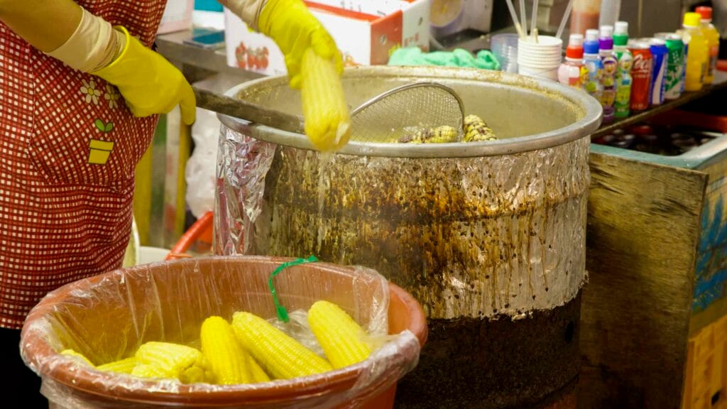 Vendor lifts corn from a simmering pot at the market stall.