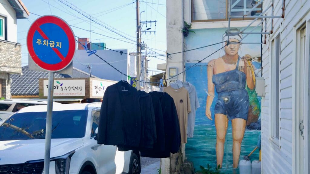 Alley with haenyeo mural and hanging clothes near the port.