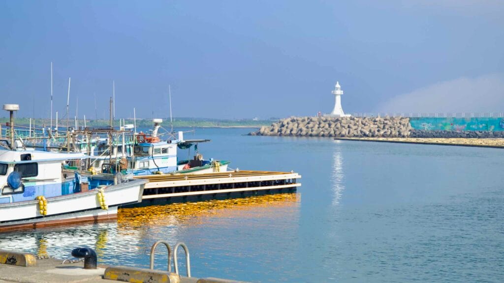 Fishing boats and a white lighthouse across the channel at Unjin Port.
