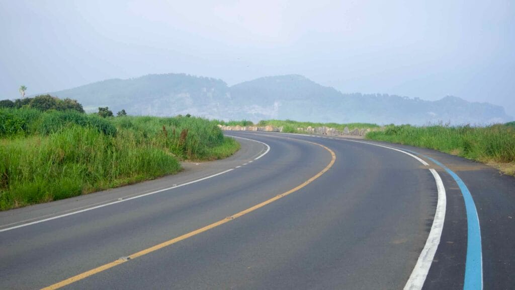 A seaside road with a blue bike‑lane stripe bends around grasses and basalt rocks.