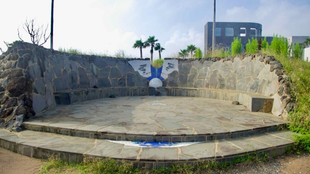 A semicircular stone amphitheater with mosaic artwork faces the sea.